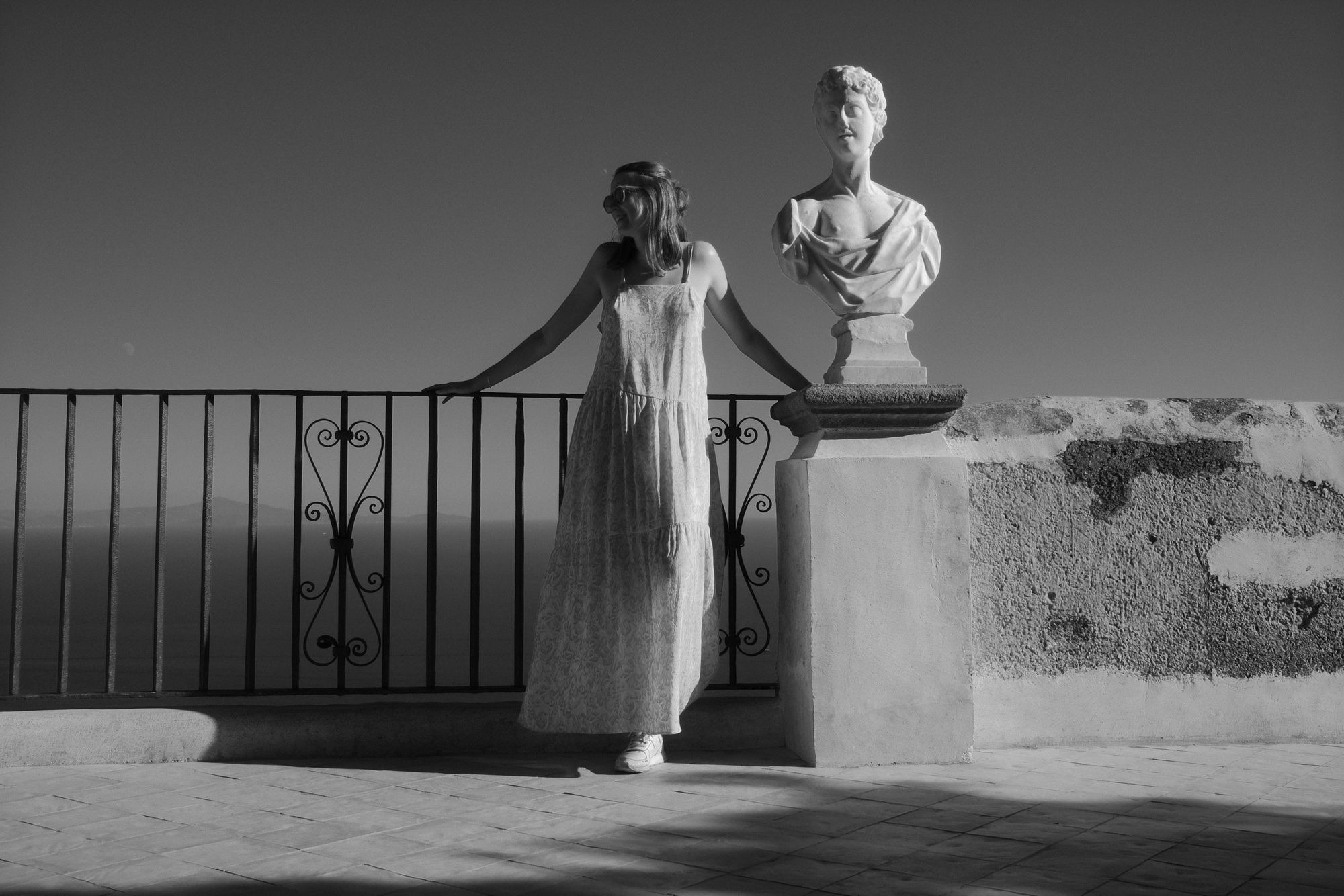 Young woman in long dress posing beside a marble bust