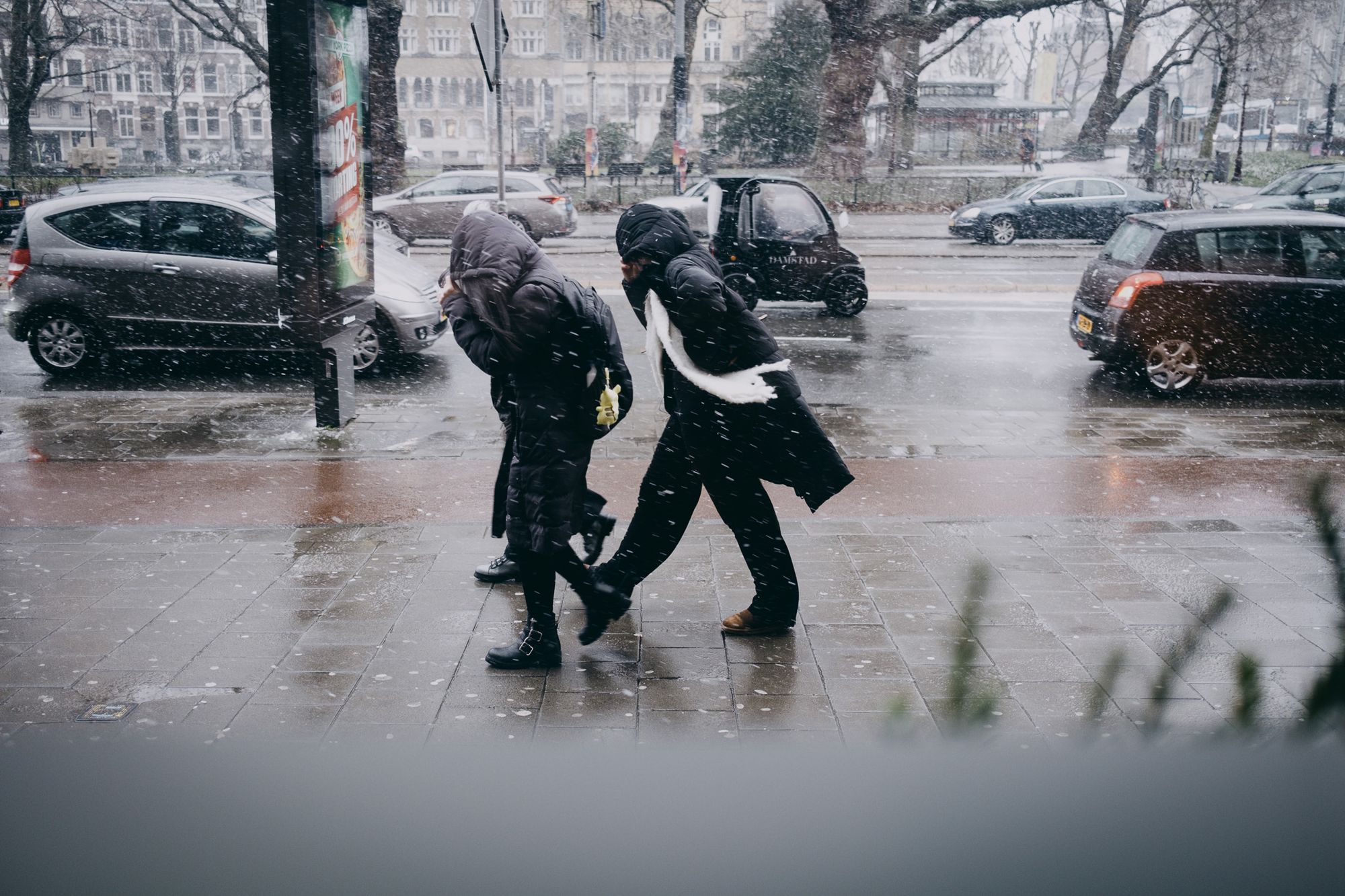 People walking against the Amsterdam rain, pulling hoods down over their face 