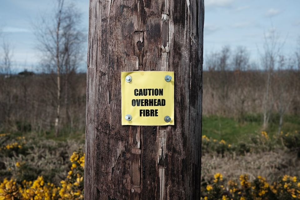 A wooden pole with a label reading ' Caution Overhead Fibre'