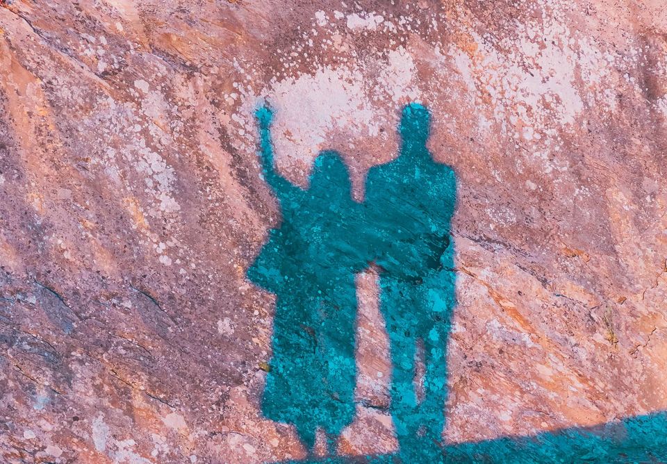 A couple casting shadows on a large rock face during sunset