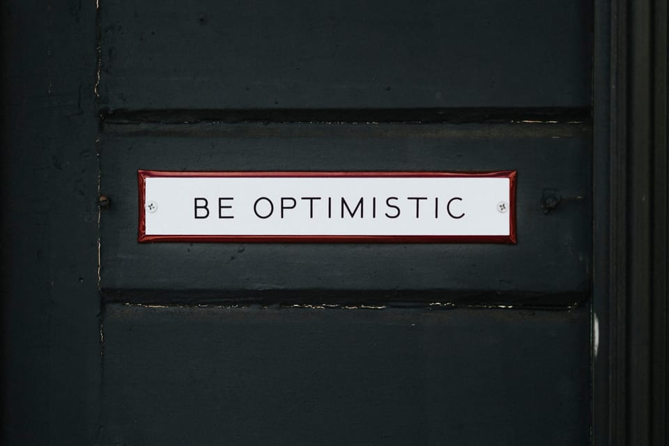 An old painted door with a notice saying "Be Optimistic".