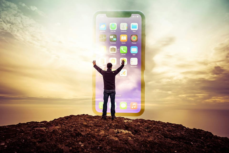 During golden hour a man stands on a rocky mound, arms outstretched and a ghostly giant iPhone stands tall before him.